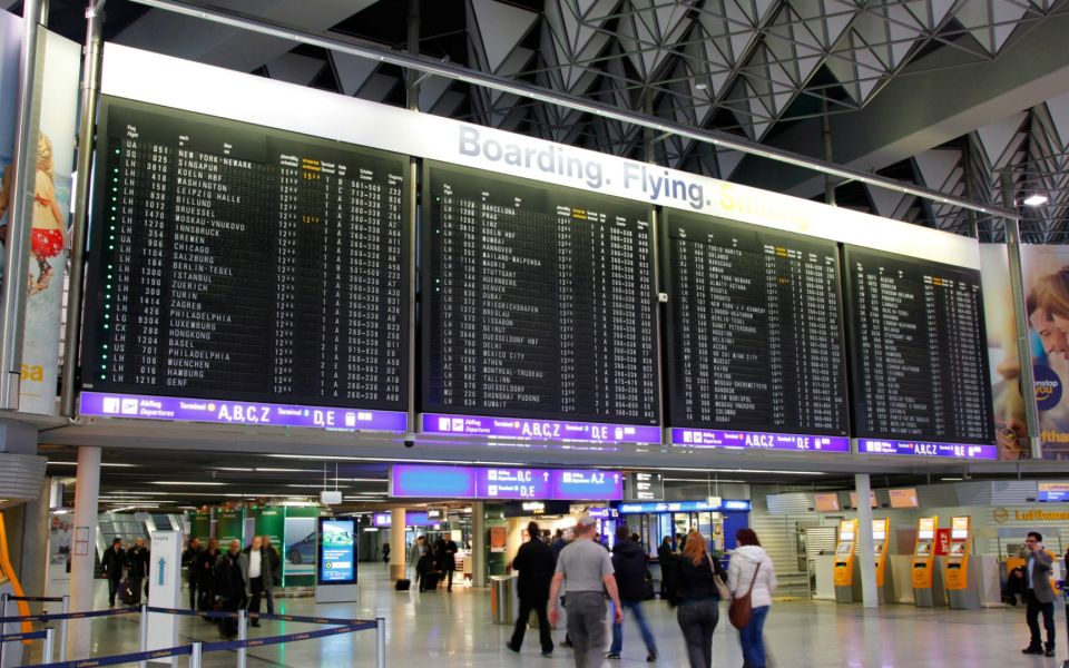 Abflughalle eines Flughafens Frankfurt mit großen digitalen Anzeigetafeln und wartenden Passagieren