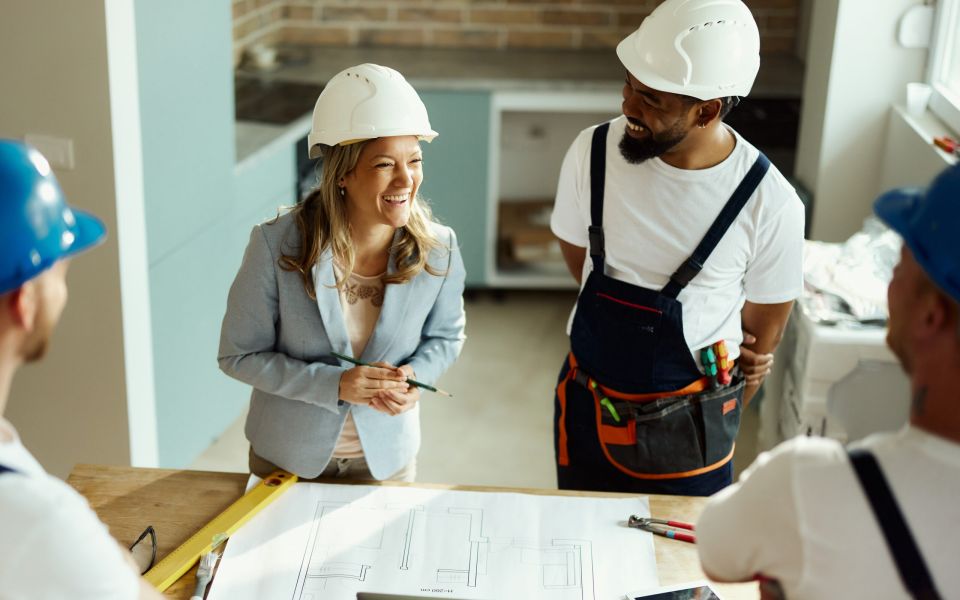 Glückliche Innenarchitektin spricht mit Handwerkern in einer Umzugswohnung