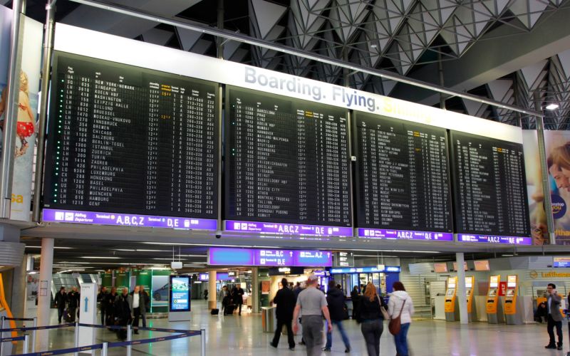 Abflughalle eines Flughafens Frankfurt mit großen digitalen Anzeigetafeln und wartenden Passagieren