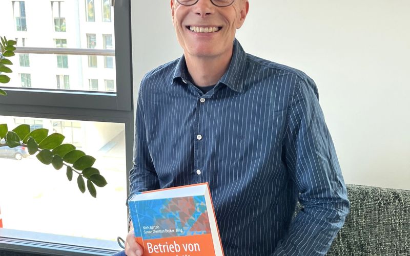Andreas Klein sitzt auf der Couch mit dem Fachbuch "Betrieb von Immobilien" in der Hand